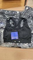 Photo showing black sports bras with bluesign approved fabric tag and snap button fasteners, individually packaged in plastic, size Small visible.
