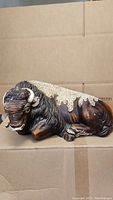 Side view of ceramic buffalo bison figurine on cardboard background showing texture and coloring