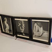 Three black framed black and white vintage nude photographic postcards displayed side by side, showing all three artworks from left to right.
