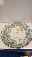 Front view of the circular glass platter showing colorful raised floral border and central winter landscape scene with person and horse.