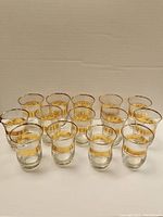 Photo showing set of 14 small vintage glasses with two gold bands near the rim on each glass.