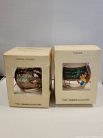 Two vintage boxed Hallmark satin ornaments side by side, showing character illustrations and text through clear box fronts