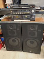 Photo showing front stacks of the tuner, amplifier, cassette deck on a table with two speakers with mesh covers in front.