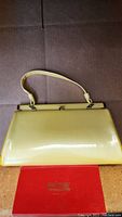 Vintage yellow handbag with short handle shown resting on brown surface with a red box in front.