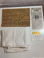 Photo of embroidery sampler, hand-quilted blanket folded, printed note, and handwritten note on table