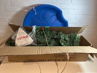 Photo of open box containing artificial Christmas tree parts and blue Pelican toboggan disc.