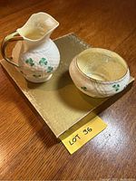 Cream colored Belleek China creamer and sugar bowl, showing shamrock pattern and gold trim, placed on a gold box.