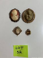 Four vintage pins on white background labeled Lot 32 including two larger cameos, one smaller cameo, and a jewelled clip.