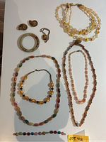 Overview of assorted jewelry including necklaces, bracelets, earrings, and bangle on white surface with lot sticker