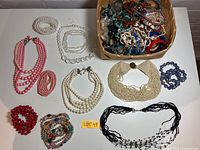 Wide view of lot showing multiple necklaces and bracelets arranged on a table with some items also in a basket.