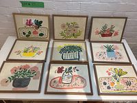 All nine framed folk art floral paintings arranged in three rows on white surface