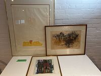 Set of three framed artworks displayed on a white surface against a white brick wall.