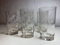 Set of six clear cylindrical highball glasses with thick bases, each engraved with cursive 'Marion & Ralph'.