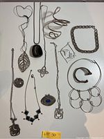 Overview of assorted silver-tone necklaces, pendants, bracelets and cuff pieces laid out on white background.