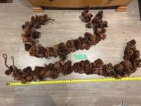 Two pine cone garlands laid flat on floor next to a tape measure that shows approximately 5 feet length each.
