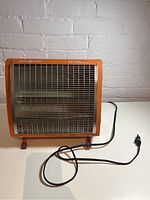 Front angled view of orange General Electric retro space heater showing metal grill, heating element, and power cord.