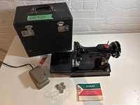 Overall view of sewing machine, case, pedal, bobbins and instruction manual on table