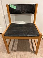 Front view of the vintage wooden chair with worn black leather upholstery on seat and backrest.