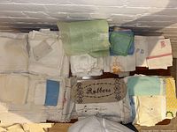 Photo of assorted folded white linens including towels, handkerchiefs, and apron pieces with lace and embroidery detail.
