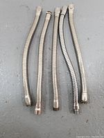 Four metal gooseneck microphone stand adapters laid out on a grey surface, showing flexible ribbed tubes with threaded ends.