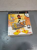 Front view of boxed Dance Dance Revolution X game accessory for PlayStation 2 showing artwork and branding.