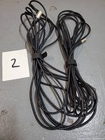 Two coiled black cables on the floor with a numbered paper '2' showing there are two cables.