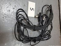 Two coiled black XLR audio cables with male and female connectors, secured with a velcro strap, displayed on a gray floor.