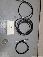 Three short black 1/4 inch mono audio cables laid out on a grey surface, showing connectors and cable length.