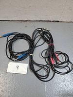 Two coiled black guitar cables with 1/4 inch connectors, one with blue and one with red shrink tubing, laying on the floor with a card labeled '9'.