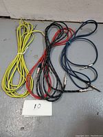Photo showing four quarter-inch guitar cables in yellow, red, black, and blue, coiled and laid on a floor with a label '10' nearby.
