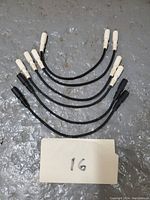 Six short RCA patch cables with white connectors and black cables, laid out on gray surface with a card labeled '16'
