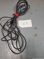 Coiled 25-foot black XLR cable with a red strap, placed on a grey floor next to a note with the number 22.