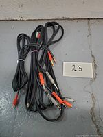 Four black audio cables with 1/4" stereo connectors and red/gray RCA connectors shown coiled on the floor next to handwritten lot number 23 sign.
