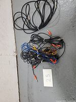 Overhead image showing bundle of multiple stereo 1/4 inch to RCA cables in black, blue, and yellow insulated wires, all tangled and tied with zip ties, with small card numbered 25 indicating quantity.