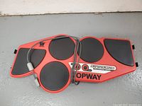 Red and black four-pad rubber drum controller for PS2 with cable wrapped on top.