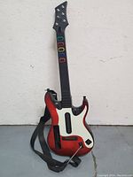 Front view of plastic guitar controller with red and white sunburst body, colored fret buttons, strap and whammy bar visible
