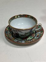 Porcelain teacup and saucer with colorful rooster design and gold trim on rims and handle.