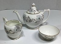 Teapot, creamer, and sugar bowl showing floral pattern and gold trim