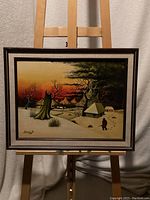 Front view of the framed painting showing the winter scene artwork hung on an easel.