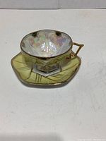 Hexagonal shaped Japanese teacup with iridescent glaze and matching saucer with greenish tones and gold trim, angled view