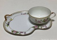 Teacup and saucer placed on a surface showing floral pattern and gold accents clearly.