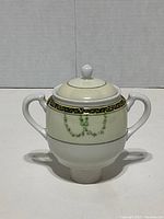 Front view of Noritake sugar bowl with lid showing dual handles and decorative border