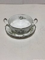 Double handled supper bowl on matching round plate showing floral pattern and silver trim