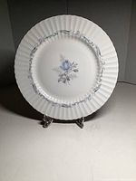 Plate showing blue rose floral design centered with decorative blue accents on scalloped edge