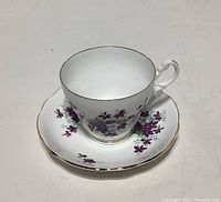 Photo showing bone china teacup and saucer with violet floral pattern and gold trim