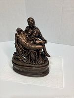 Front view of the Pieta sculpture showing Mary holding Jesus, bronze color, with inscription on base.