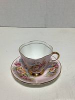 Front view of the teacup placed on the saucer showing floral pattern and gilded details on handle and foot.