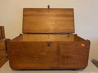 Open wooden trunk showing natural wood interior, hinged lid, and front latch