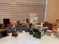 Full view of assorted dollhouse furniture and dolls arranged on white surface in front of blinds