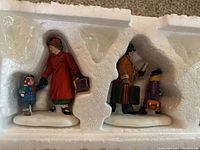 Top view of four Department 56 Home For Holidays carolers figurines in original foam packaging showing detailed paint and accessories